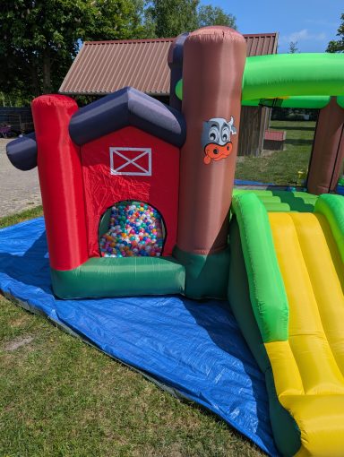 Unsere kleine Farm Bunte Hüpfburg mit Rutsche, angrenzend an einen Bereich mit bunten Bällen.